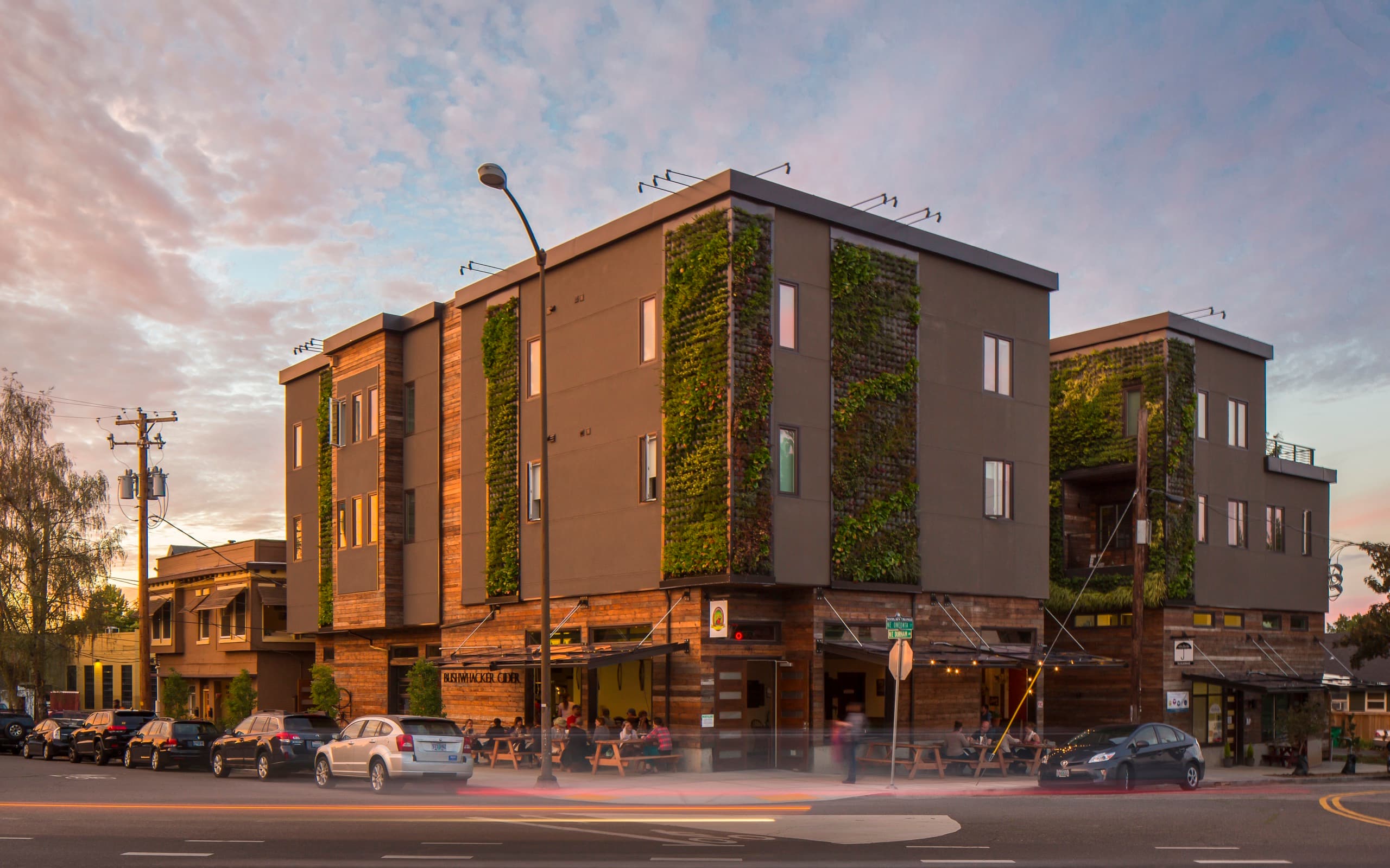 Woodlawn at dusk in Portland, a four-story building with vertical living walls over busy ground-floor retail